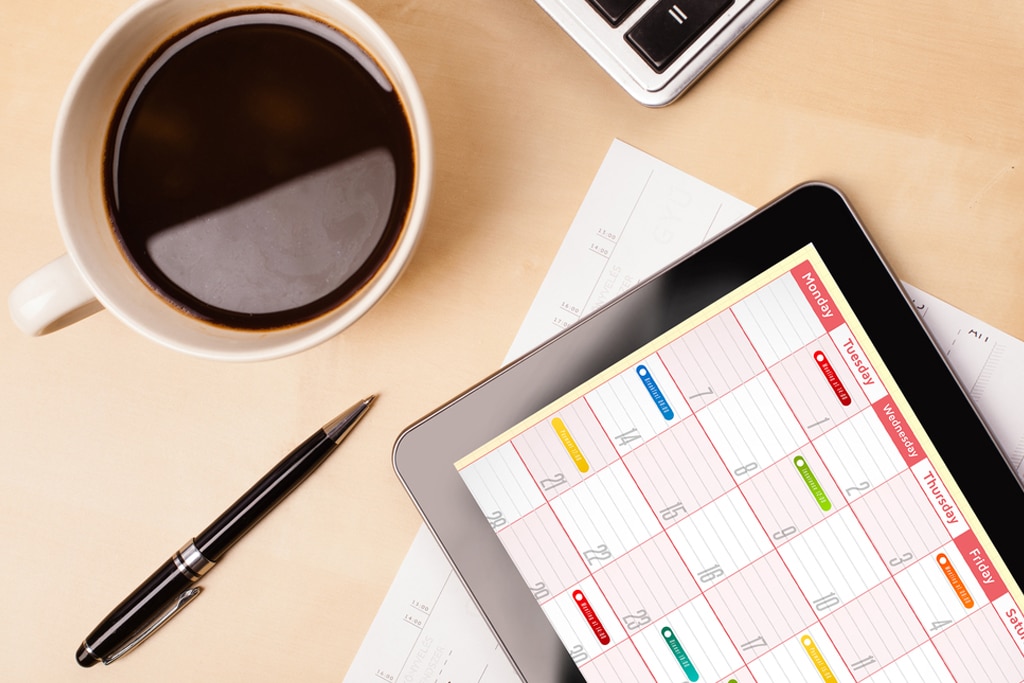 Workplace with tablet pc showing calendar and a cup of coffee on a wooden work table close-up Workplace with tablet pc showing calendar and a cup of coffee on a wooden work table close-up